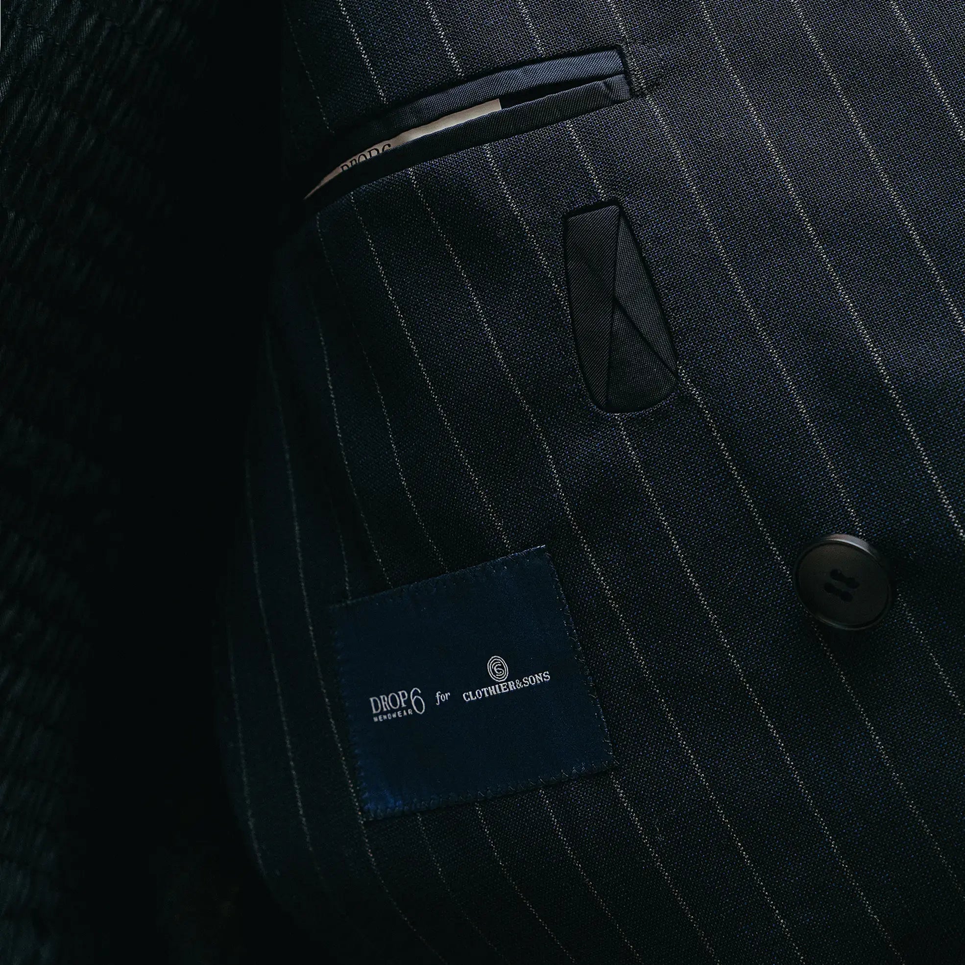 Fabric label detail of the Drop6 Wool Chalk Stripe Double Breasted Suit Navy showing the cloth tag, chalk stripe wool fabric, and material identification for Clothier & Sons.