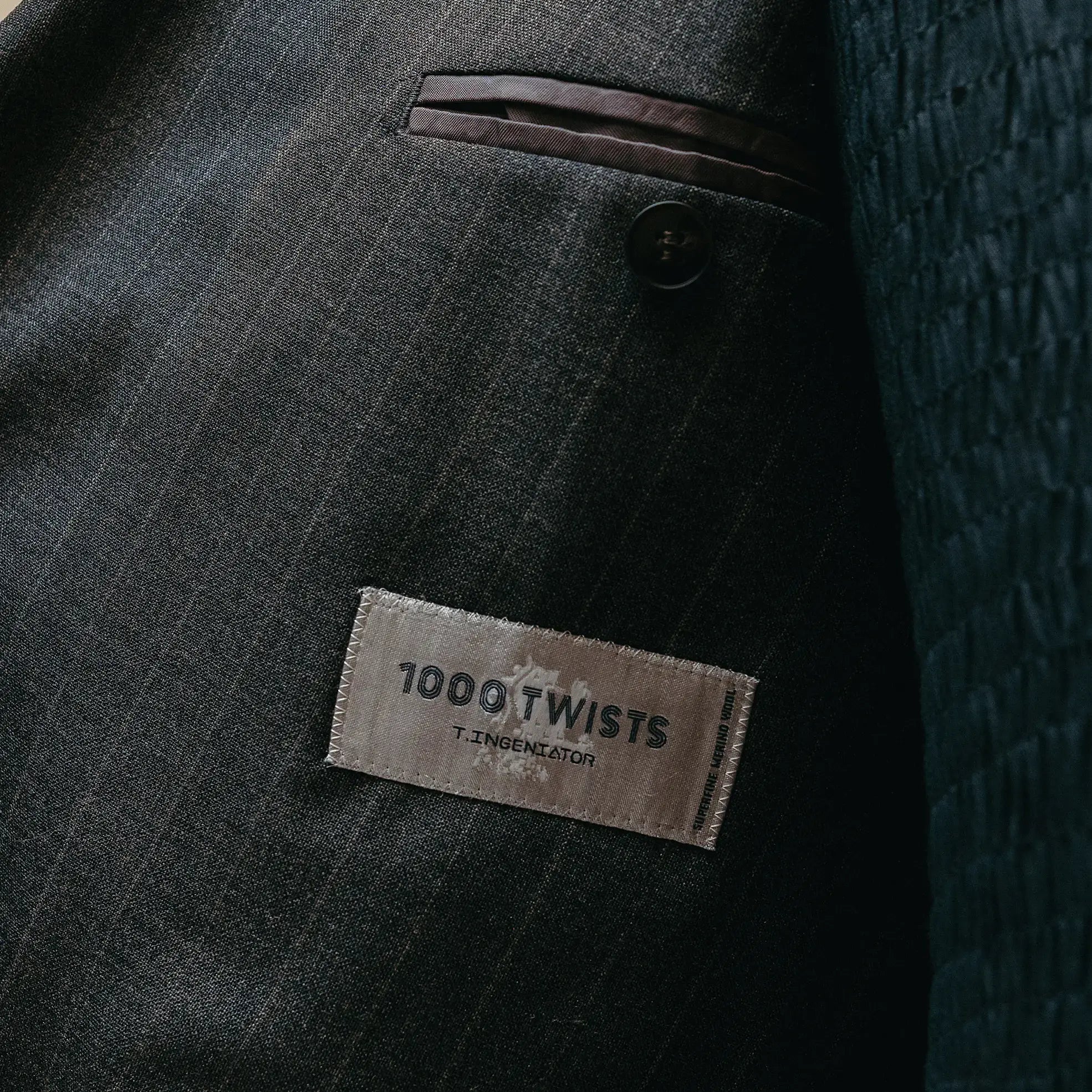 Fabric label detail of the Drop6 Wool Chalk Stripe Double Breasted Suit Charcoal Grey showing the cloth tag, chalk stripe wool fabric, and material identification for Clothier & Sons.